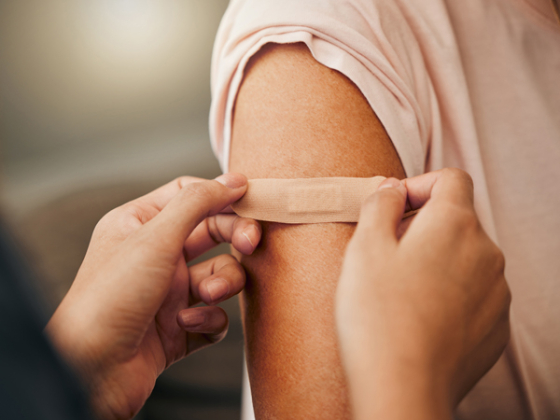 Someone putting a bandaid on the arm of another person. Credit: AdobeStock