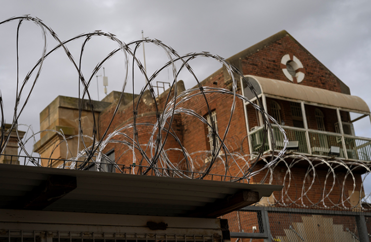 Barbed wire in foreground and brick prison building in background