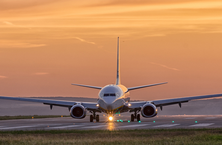 A plane lands on a runway with an orange sky in background